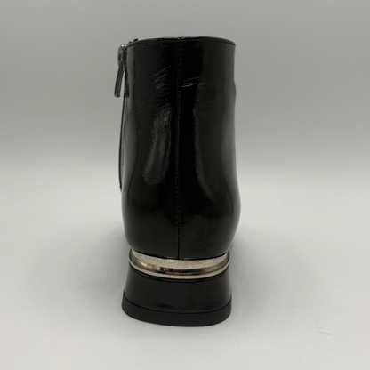 A black patent leather ankle boot shown from the back, featuring a silver metallic ring accent around the base of the block heel.
