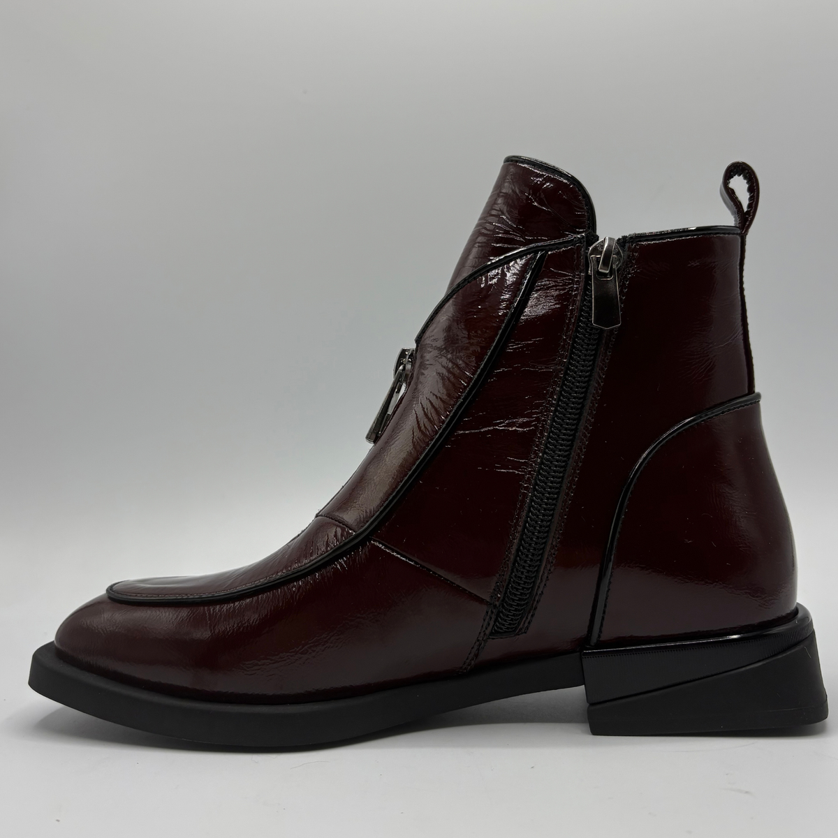 Left facing view of a deep red patent leather short boot with a side and front zipper