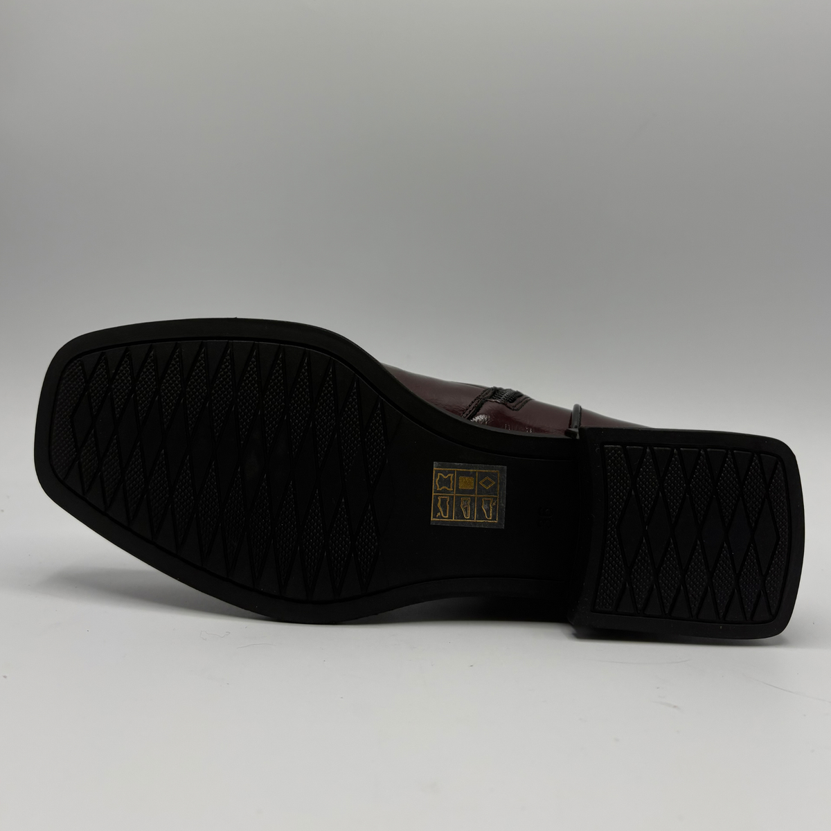 Bottom view of a deep red patent leather short boot with a black rubber outsole