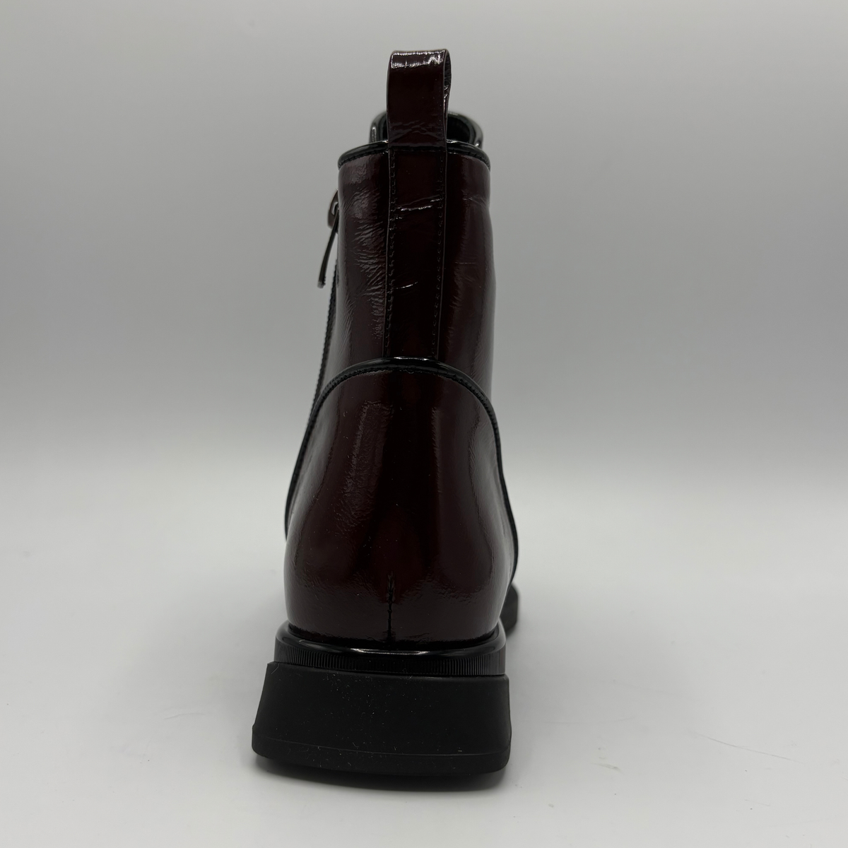 Back view of a deep red patent leather short boot with a pull on heel tab