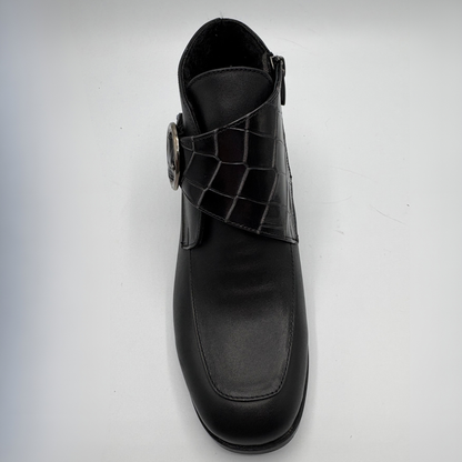 Top view of a black leather ankle boot with a croc textured strap and a circular buckle