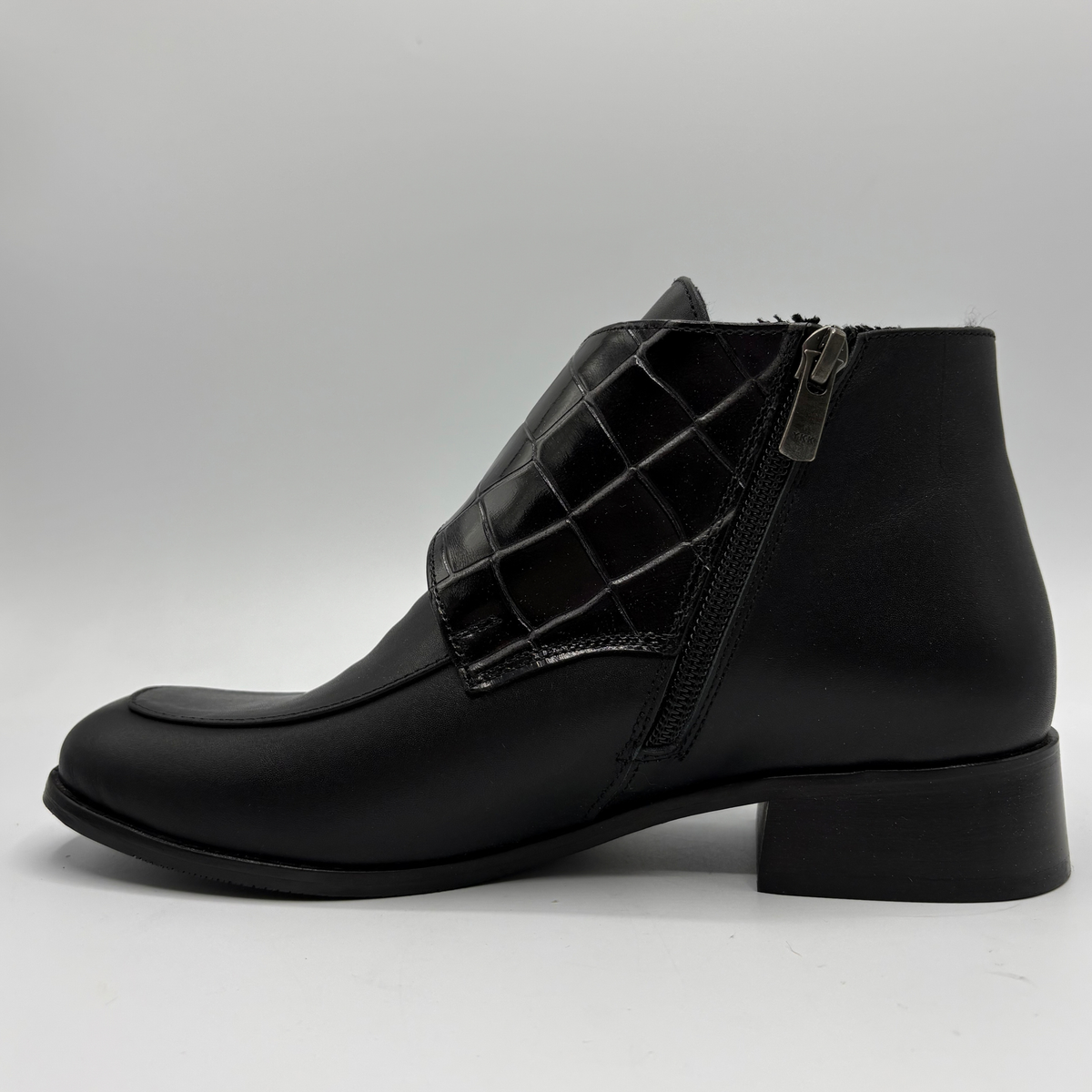 Left facing view of a black leather ankle boot with a croc textured strap and a circular buckle