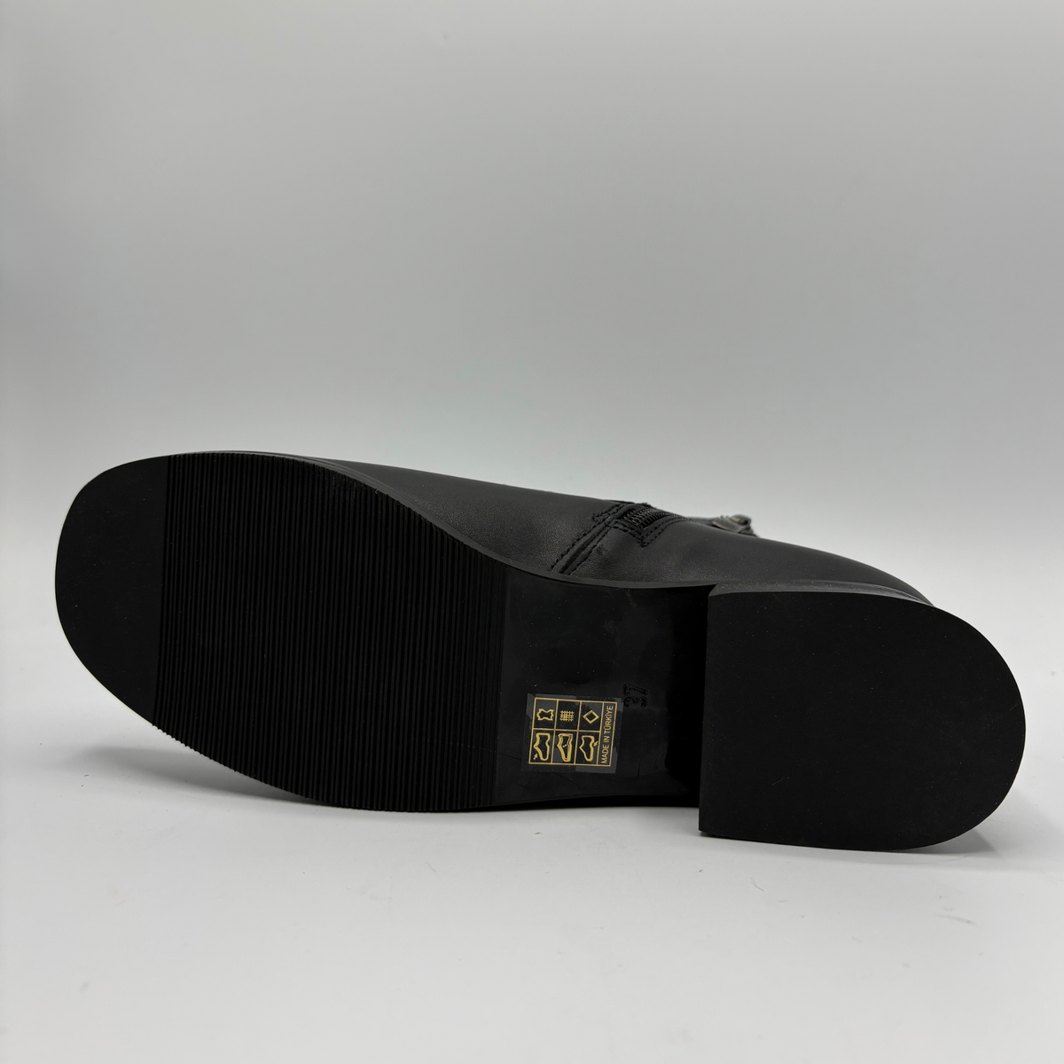 Bottom view of a black leather ankle boot with a croc textured strap and a circular buckle
