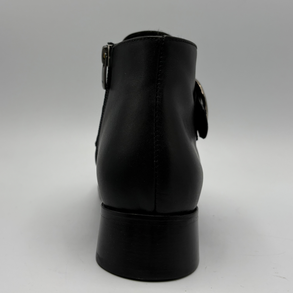 Back view of a black leather ankle boot with a croc textured strap and a circular buckle