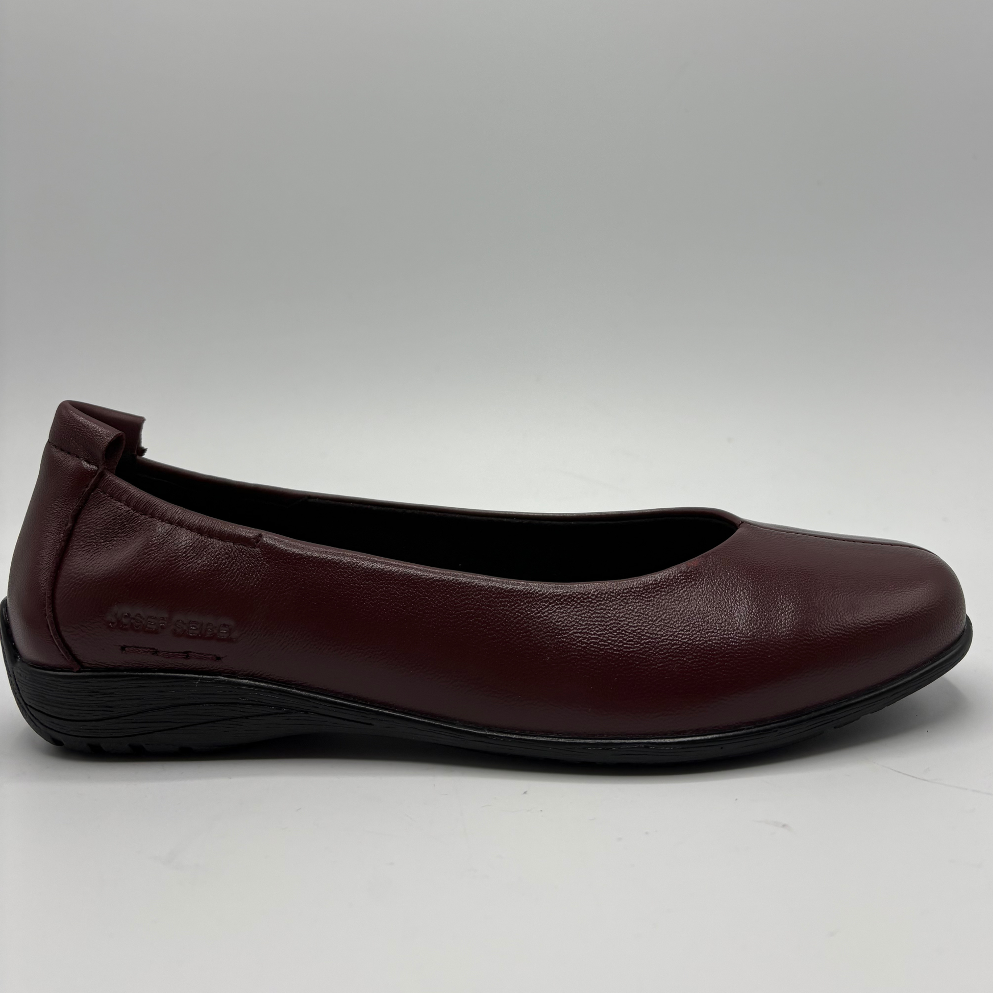 A single women's flat shoe in burgundy leather with a black sole, shown from a side profile view against a light gray background.