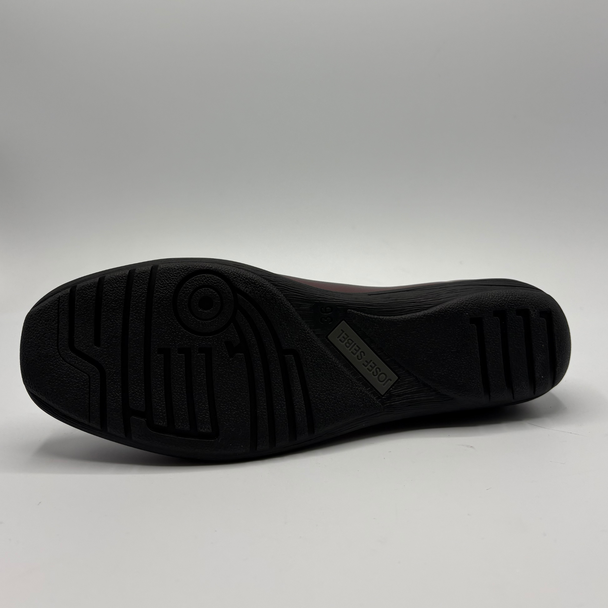 The black rubber outsole of a shoe, showing tread patterns and a small 'D'NUEVO' brand tag, photographed against a neutral gray studio background.