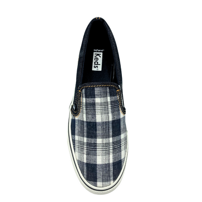 Top down view of a canvas slip on sneaker by Keds.  Black plaid on the top and denim around the heel