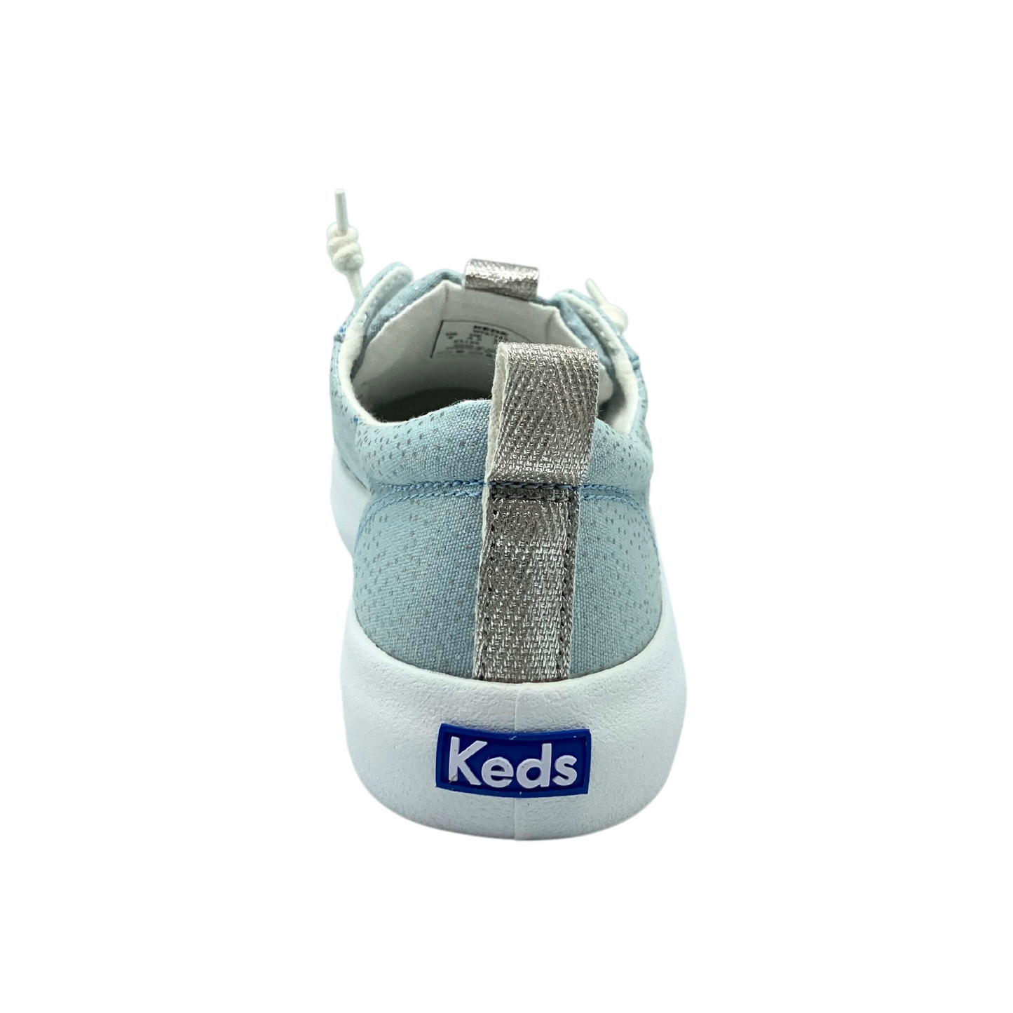 Rear view of a slip on sneaker in a light blue canvas with a silver tab at the back.  White outsole with Keds logo at the heel