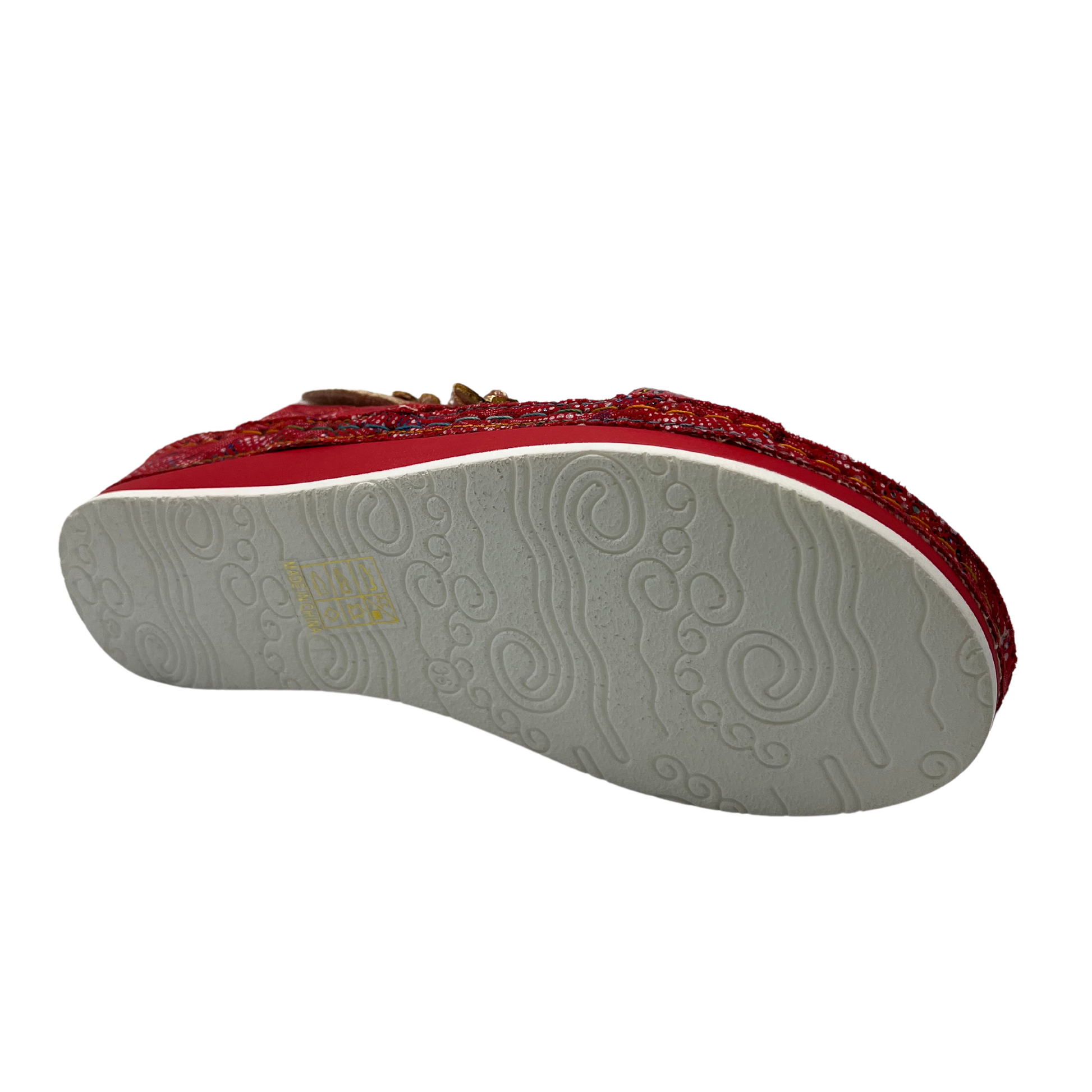 Bottom view of a red leather sandal with flower details and velcro ankle strap