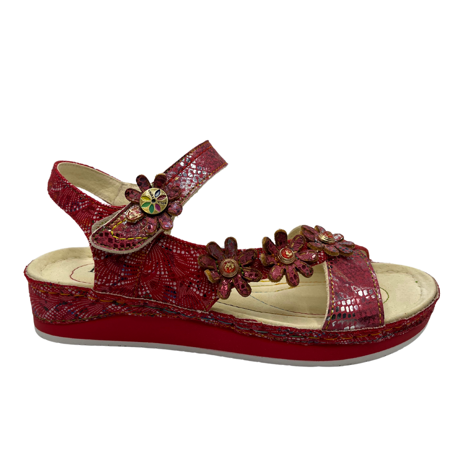 Right facing view of a red leather sandal with flower details and velcro ankle strap