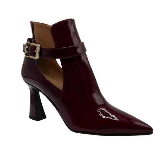 45 degree angled view of merlot patent leather bootie with a flared heel and pointed toe. Ankle strap with gold buckle and leather lined interior.