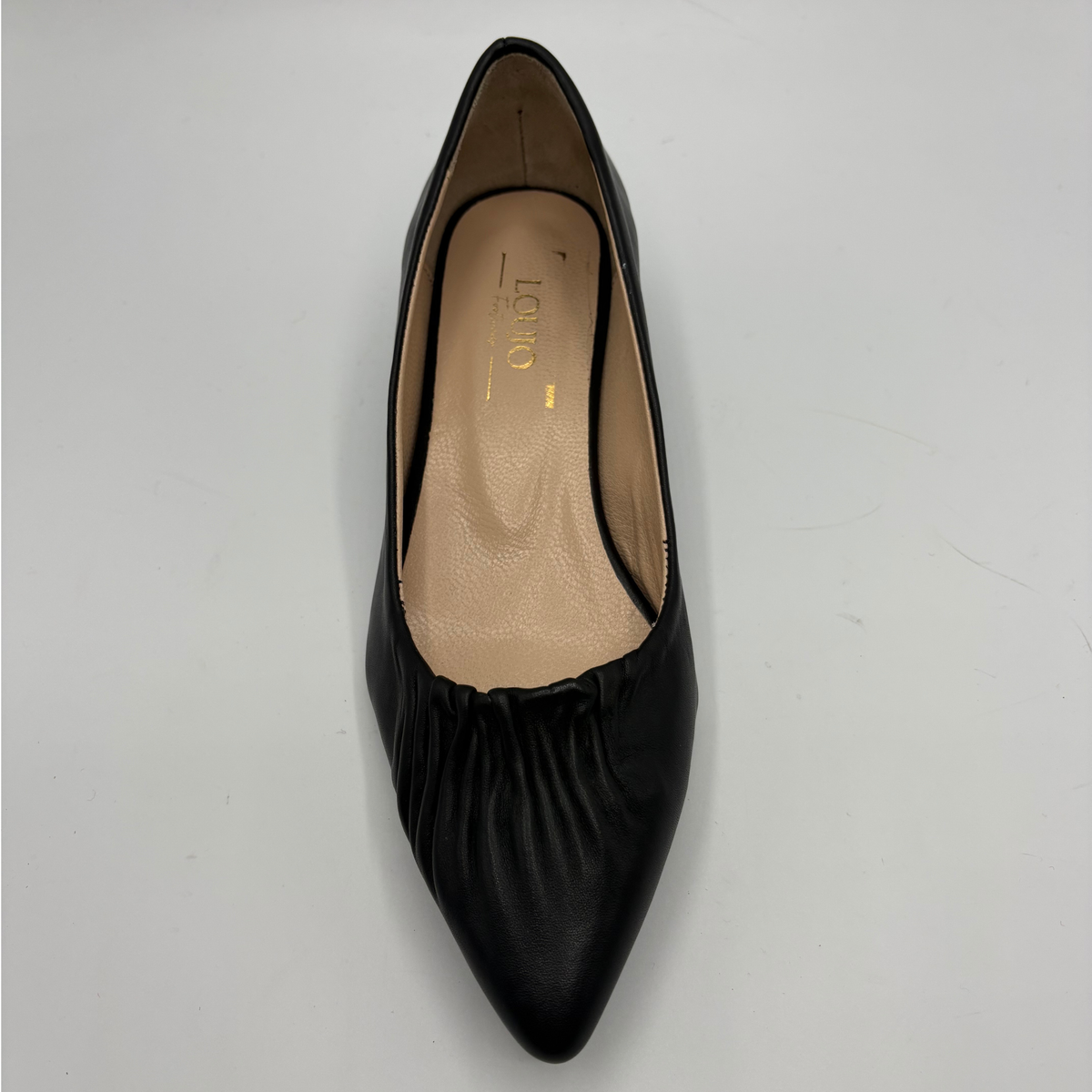 Top view of a black leather pump with a slouchy accent on the pointed toe and a gold accent on the heel