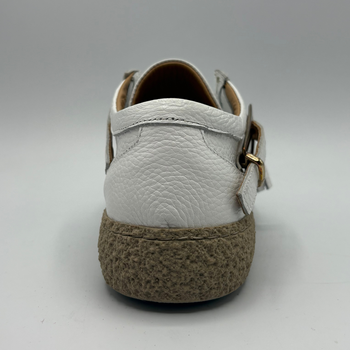Back view of a white leather shoe with a rubber outsole and a buckle closure