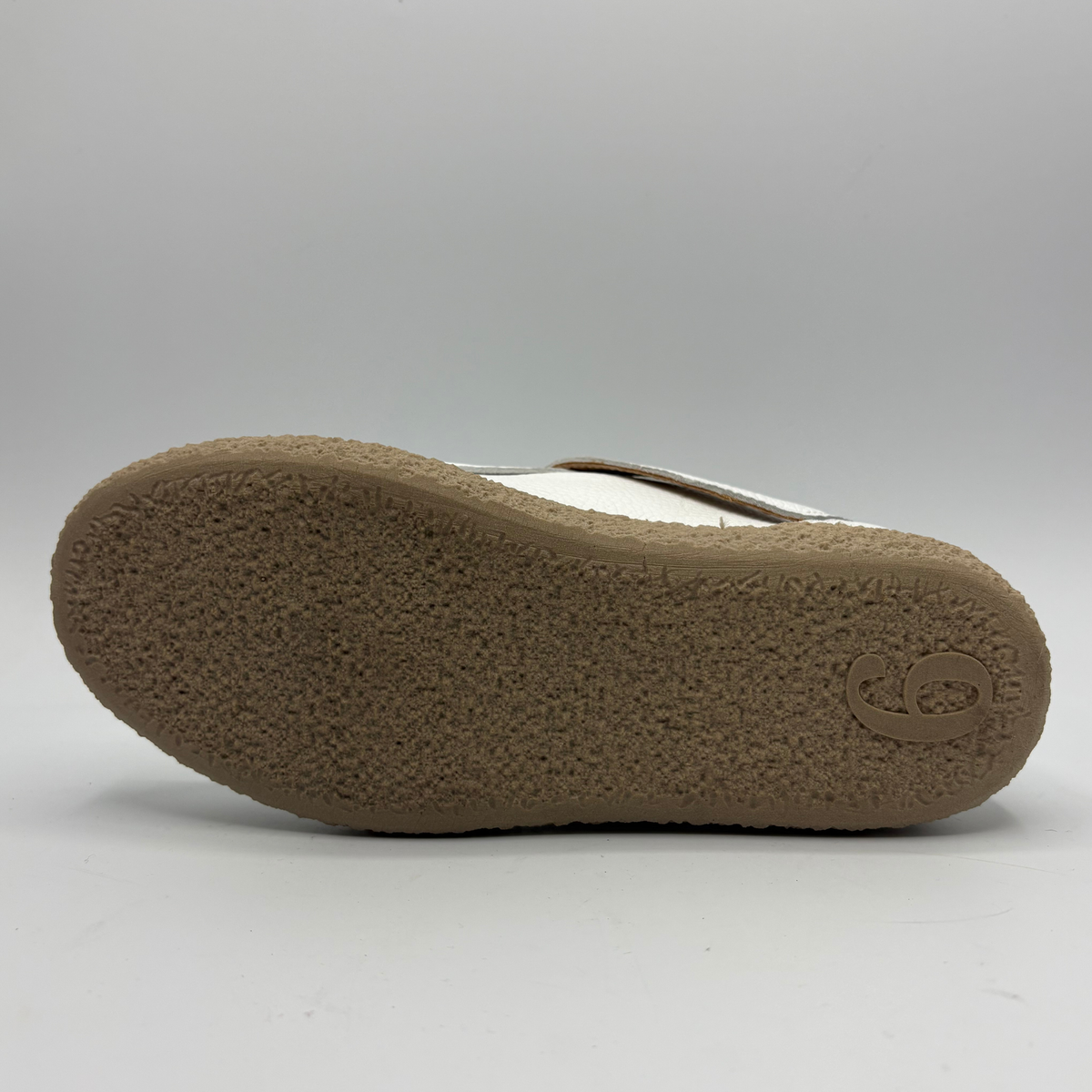 Bottom view of a white leather shoe with a rubber outsole and a buckle closure