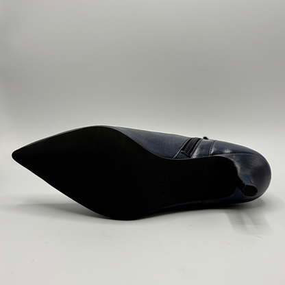 A single navy blue pointed-toe shoe shown from a side angle, displaying its black sole and a small side zipper, set against a plain light gray studio background.