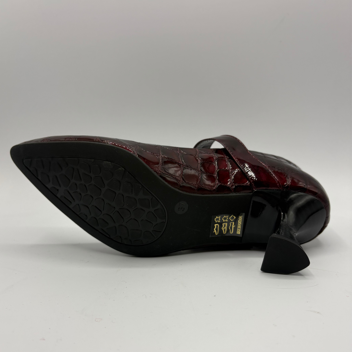 Bottom view of a burgundy high heeled shoe with a flared heel and gold buckle
