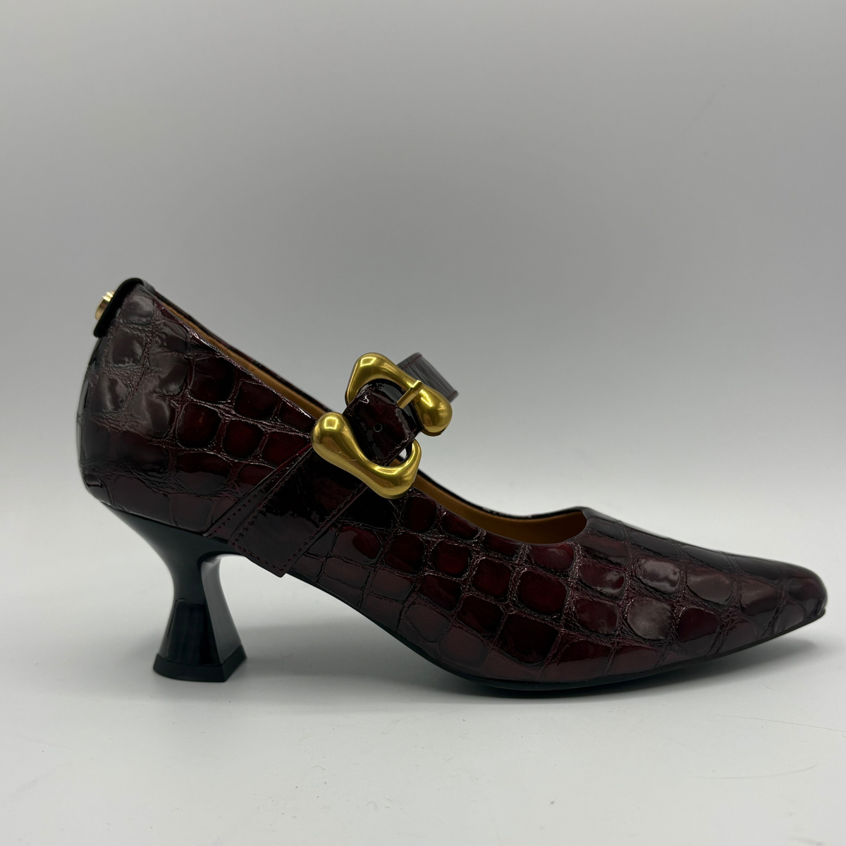 Right facing view of a burgundy high heeled shoe with a flared heel and gold buckle