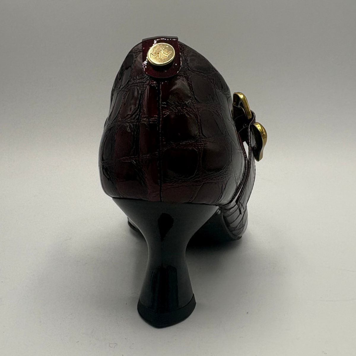Back view of a burgundy high heeled shoe with a flared heel and gold buckle