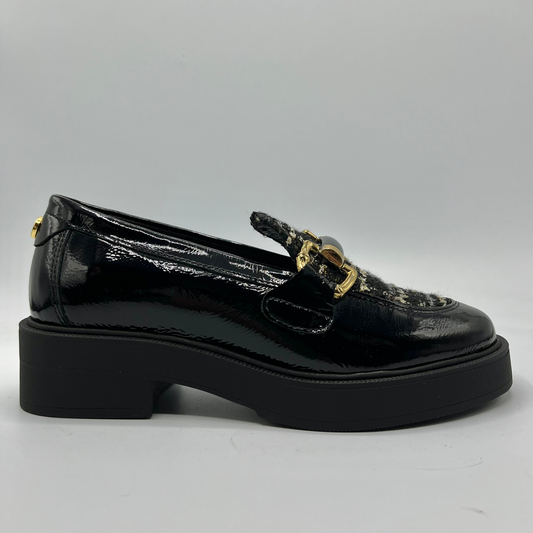 Black patent leather loafer with gold buckle on a gray background