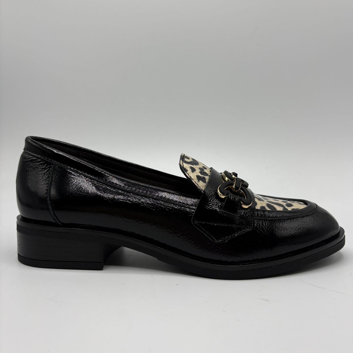 Right facing view of a black leather loafer with an animal print accent on the toe box and chain detail.