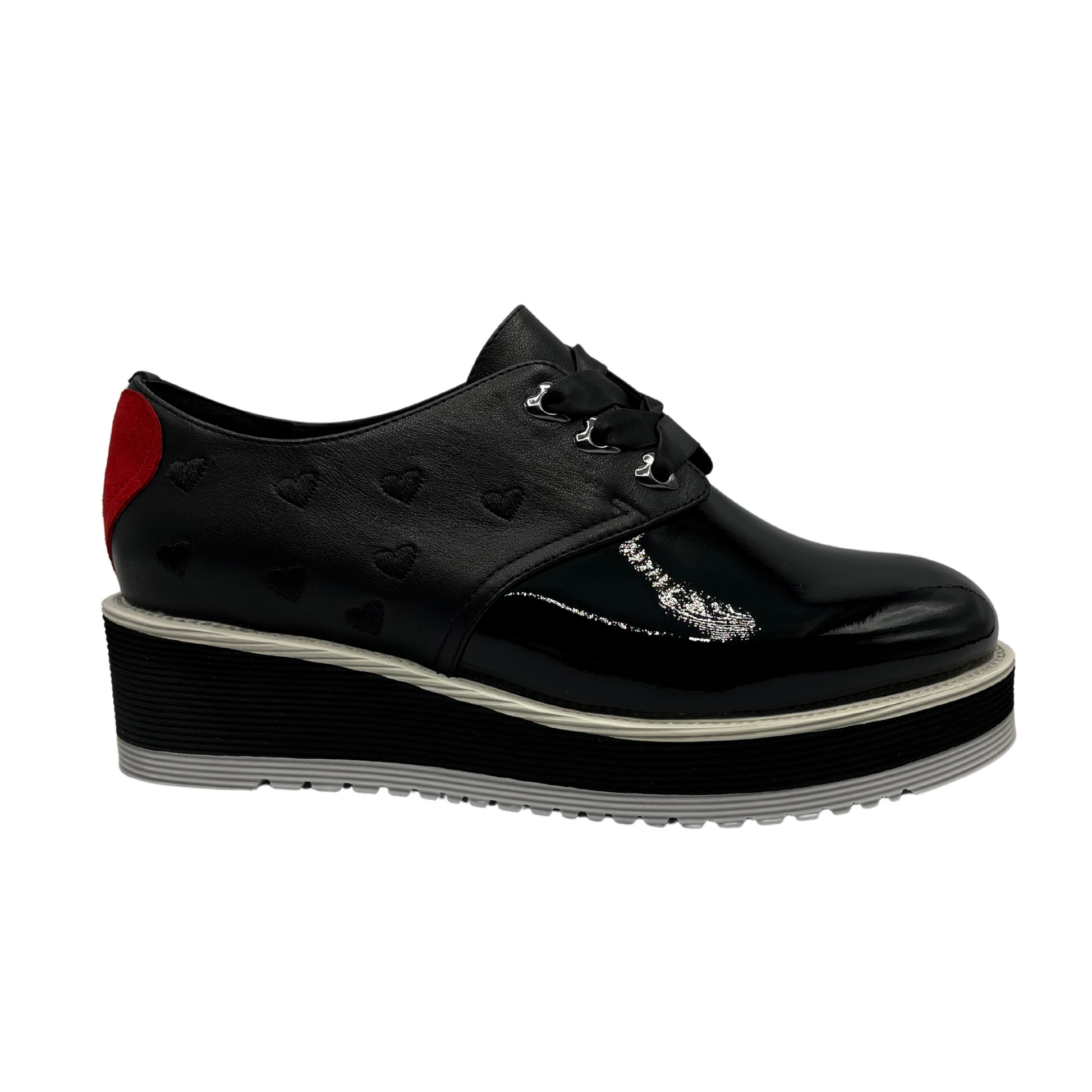 Right facing view of black patent leather shoe with red heart on the heel, ribbon laces and thick rubber outsole.