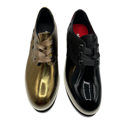 Top view of two leather shoes beside each other. One is gold and one is black. Both have matching ribbon laces and heart details