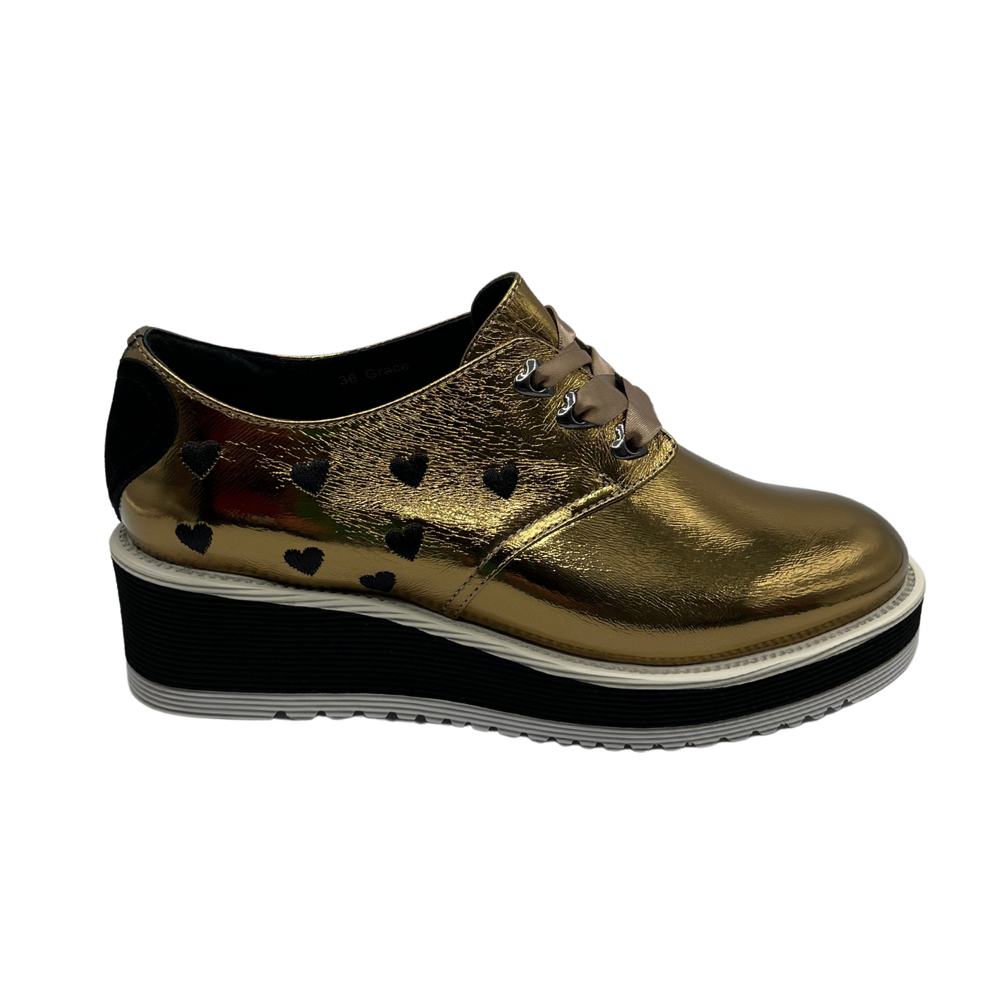 Right facing view of gold patent leather shoe with a black heart on the heel, ribbon laces and thick rubber outsole.