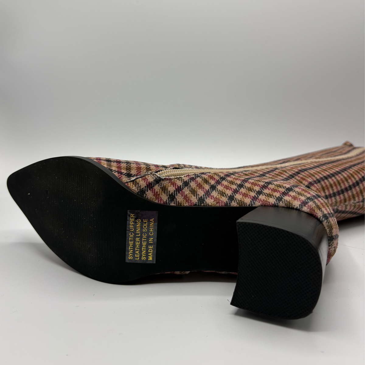 A knee-high pointed-toe boot with a black block heel, featuring a red, black, and white plaid pattern on a clean white background.