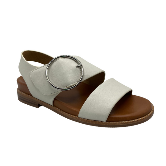 45 degree angled view of white leather strapped sandals with tan leather lining. Large round silver buckle and low heel