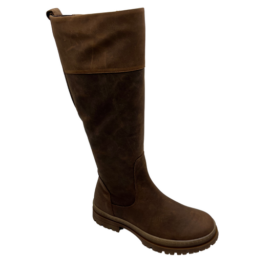 45 degree angled view of leather tall boot with lug outsole, pull on heel tab and inside zipper.