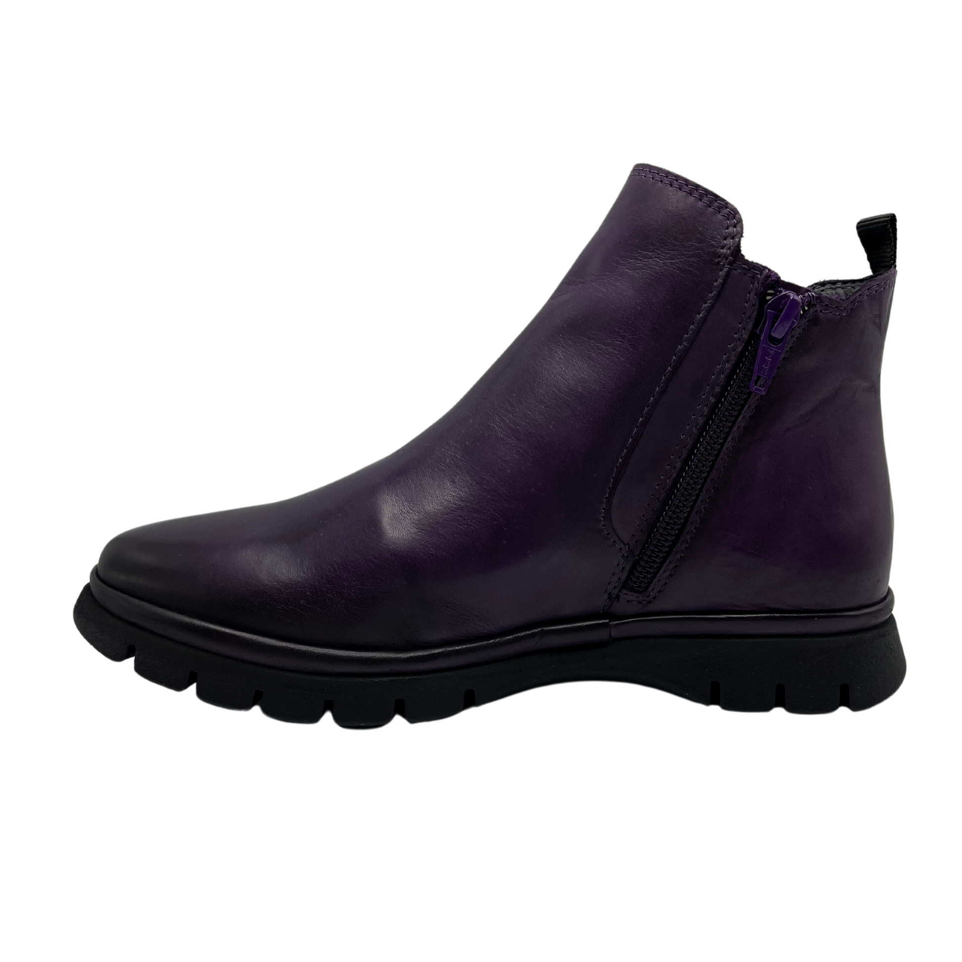 Left facing view of dark purple leather short boot with slim black outsole and pull on heel tab. Elastic side gore with rounded toe