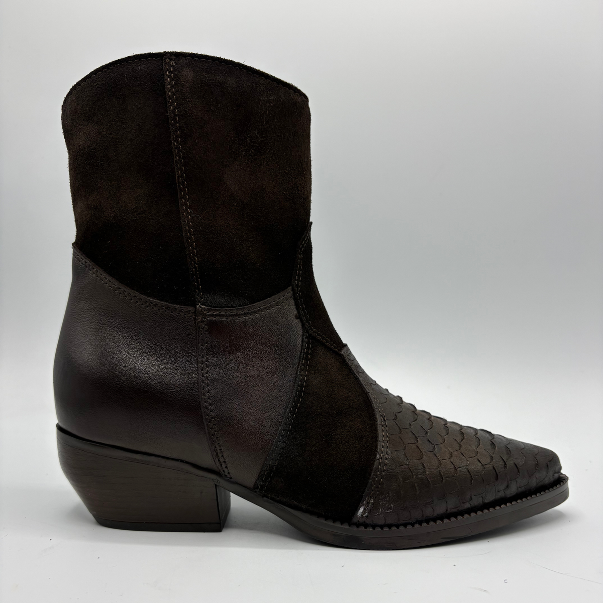 A dark brown western-style ankle boot featuring a mix of smooth leather panels and a textured woven leather toe cap, set against a plain light gray background.