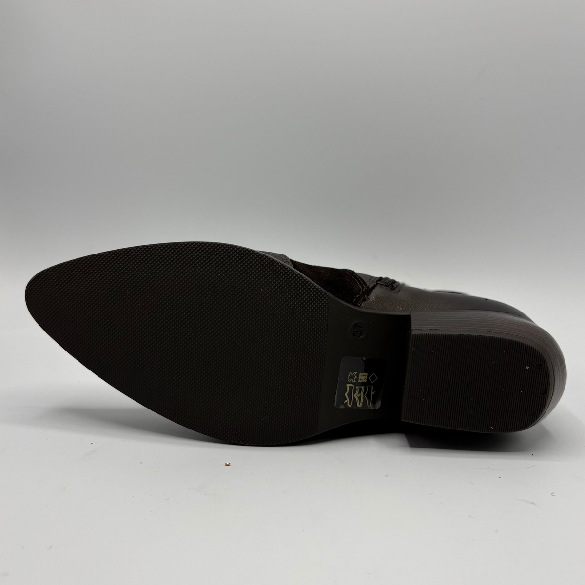 A close-up of the black rubber outsole of a dark brown boot, showing the brand name on the heel area, set against a neutral gray background.