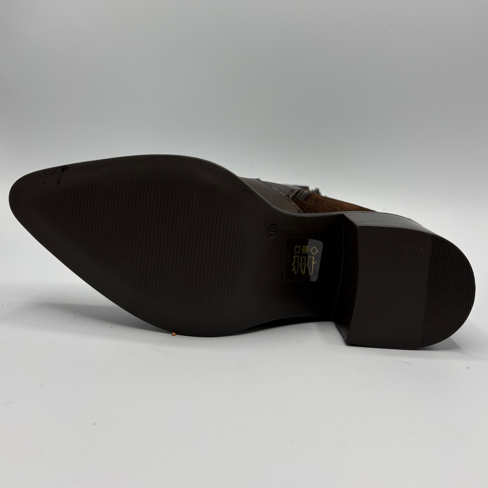 The sole of a dark brown leather boot, showing a pointed toe and a textured black rubber outsole