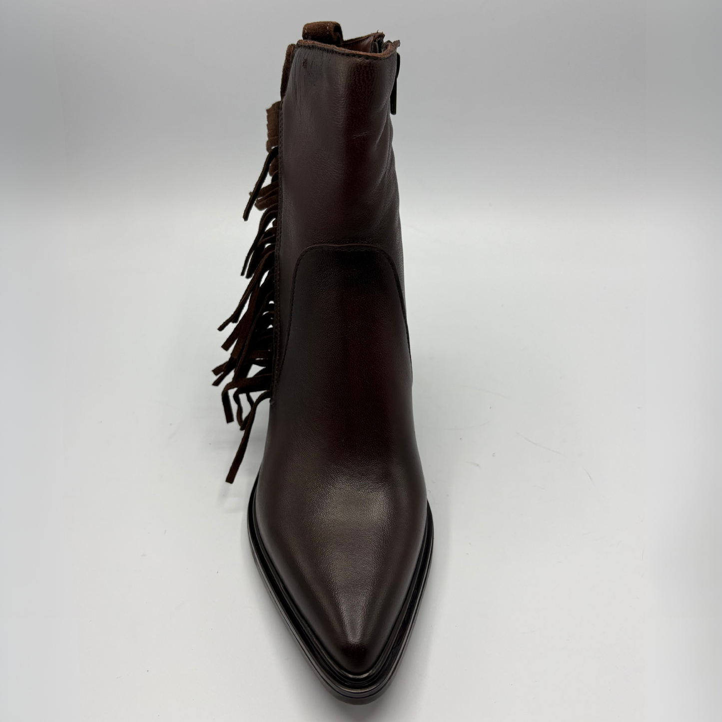 A dark brown leather ankle boot with a pointed toe and fringe detailing along the side, photographed against a neutral light gray background.