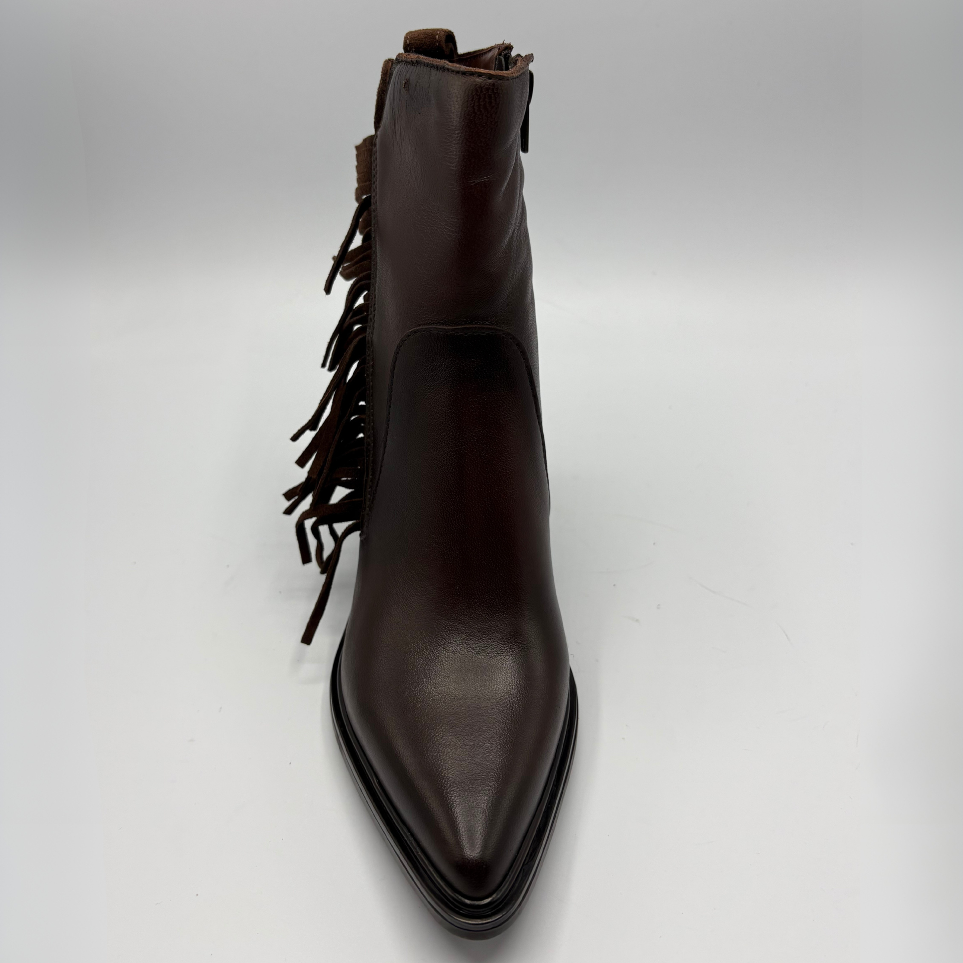A dark brown leather ankle boot with a pointed toe and fringe detailing along the side, photographed against a neutral light gray background.