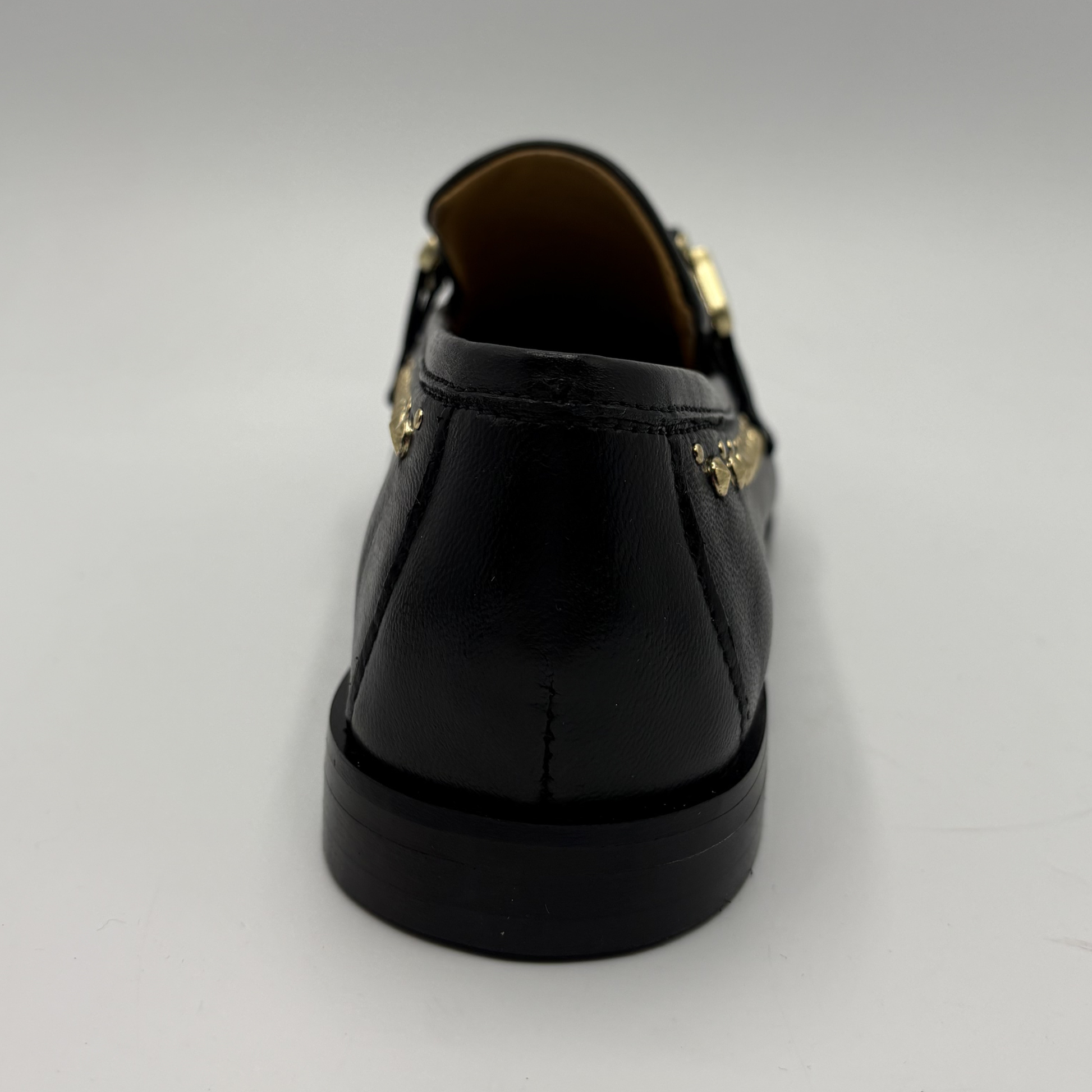 Black leather shoe with gold accents on a light gray background