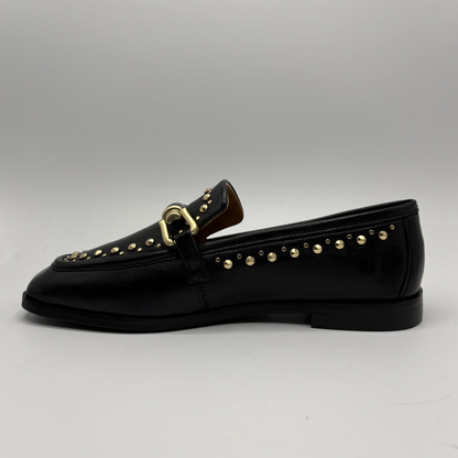 Black loafer with gold studs and buckle on a gray background
