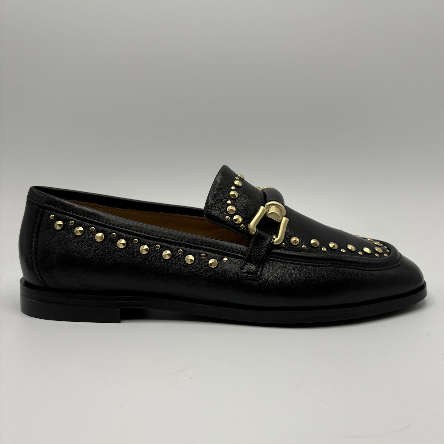 Black loafer with gold studs and buckle on a gray background