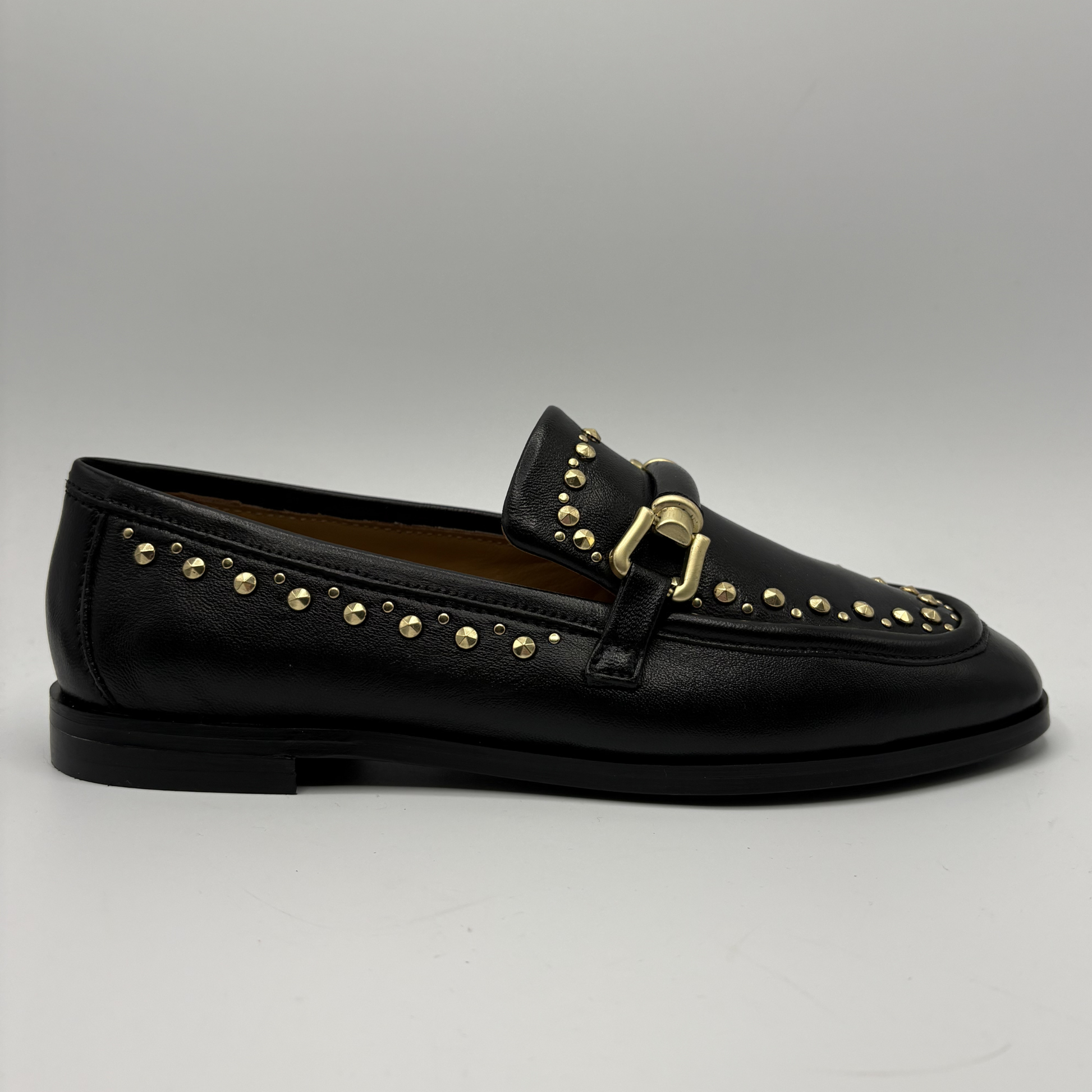 Black loafer with gold studs and buckle on a gray background