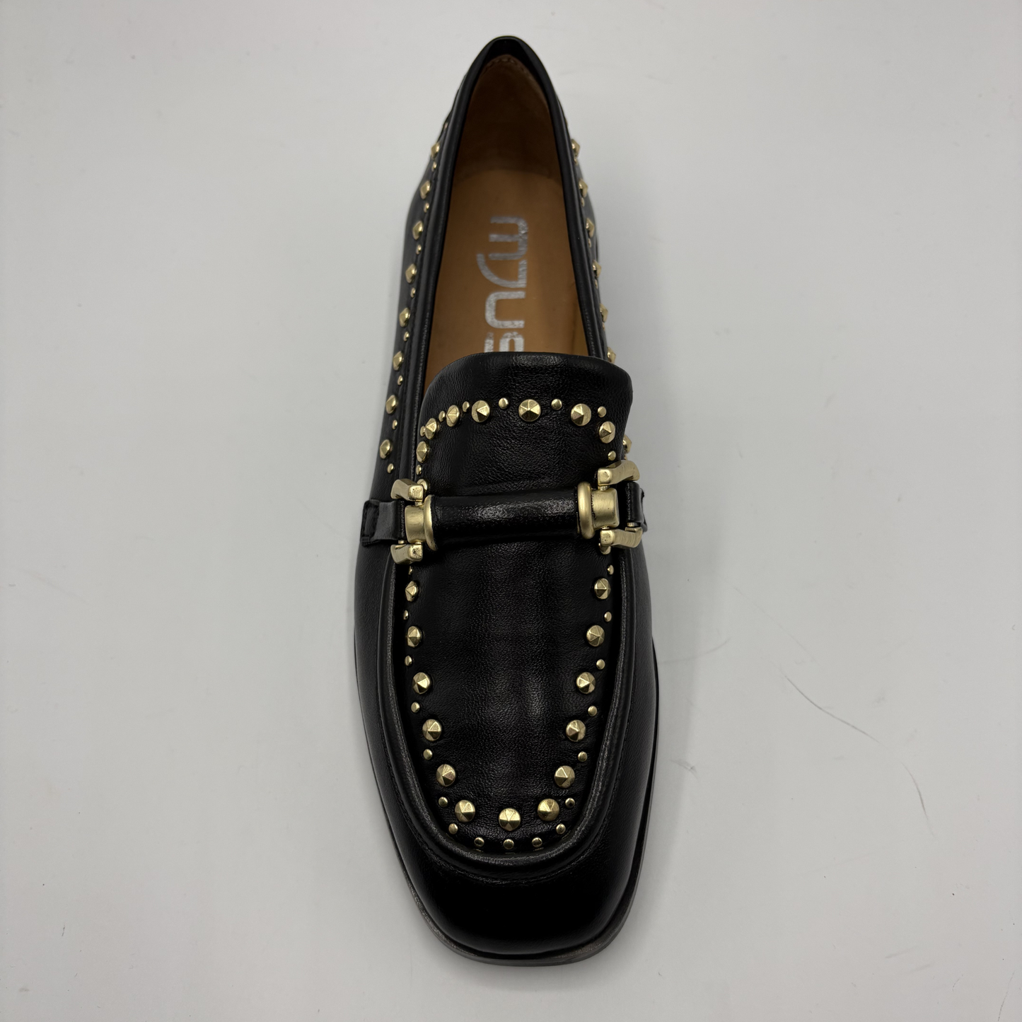 Black loafer with gold studs on a light gray background