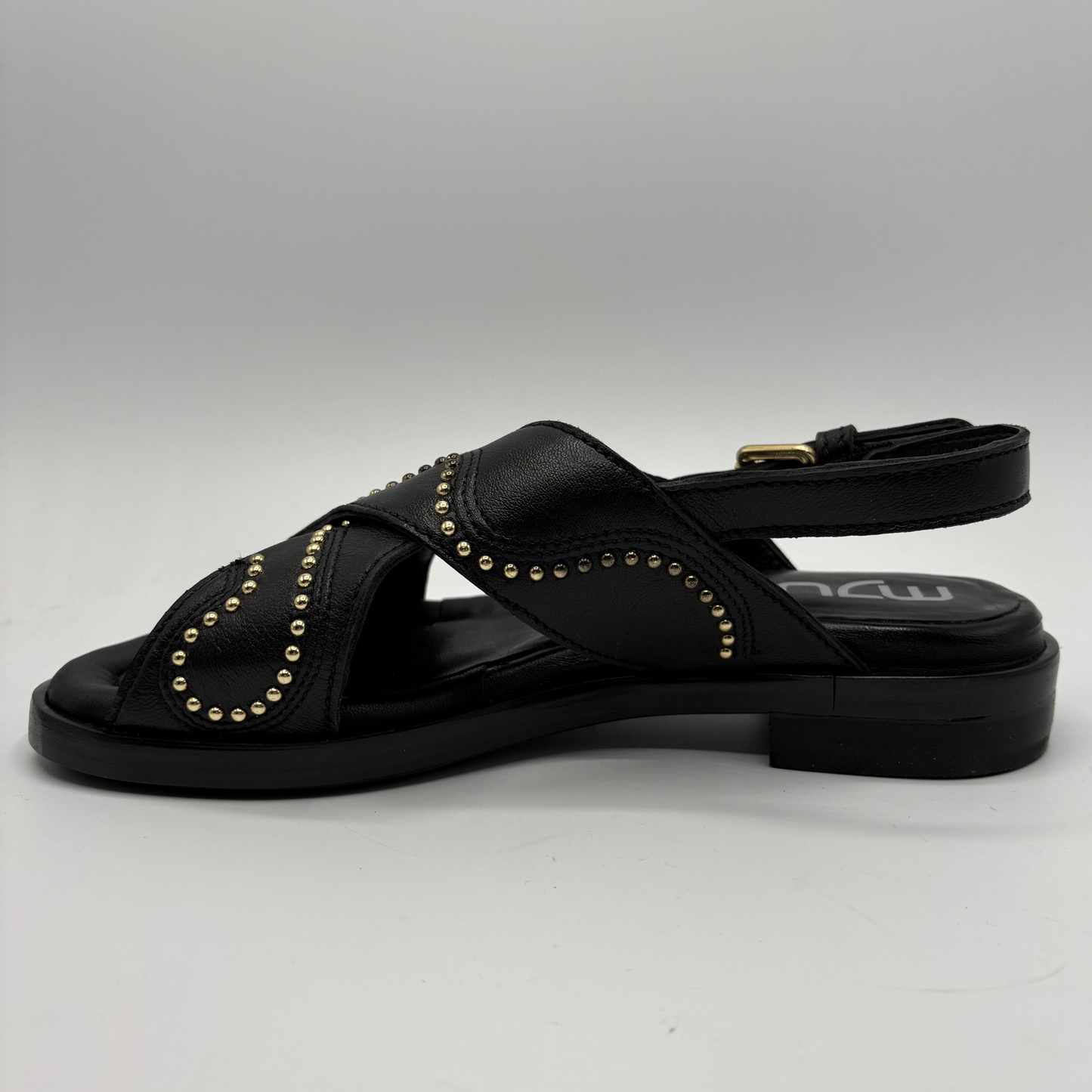 Black sandal with gold studs on a gray background