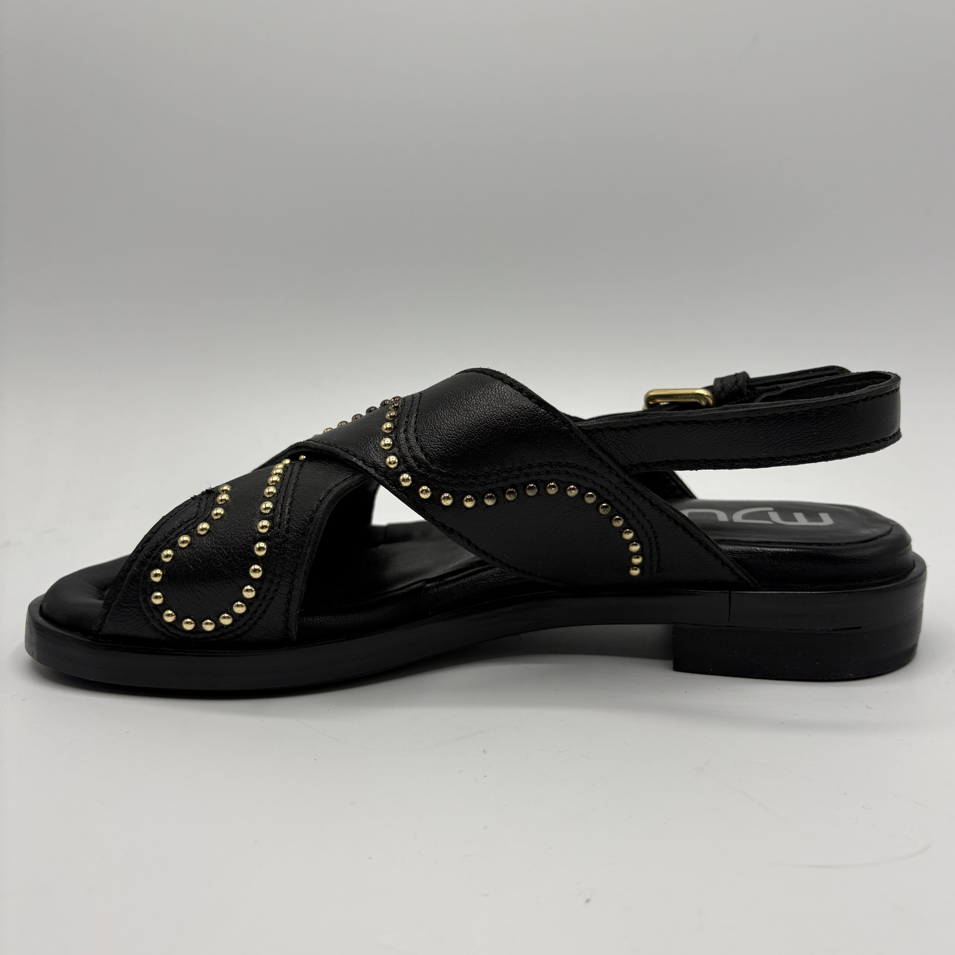 Black sandal with gold studs on a gray background