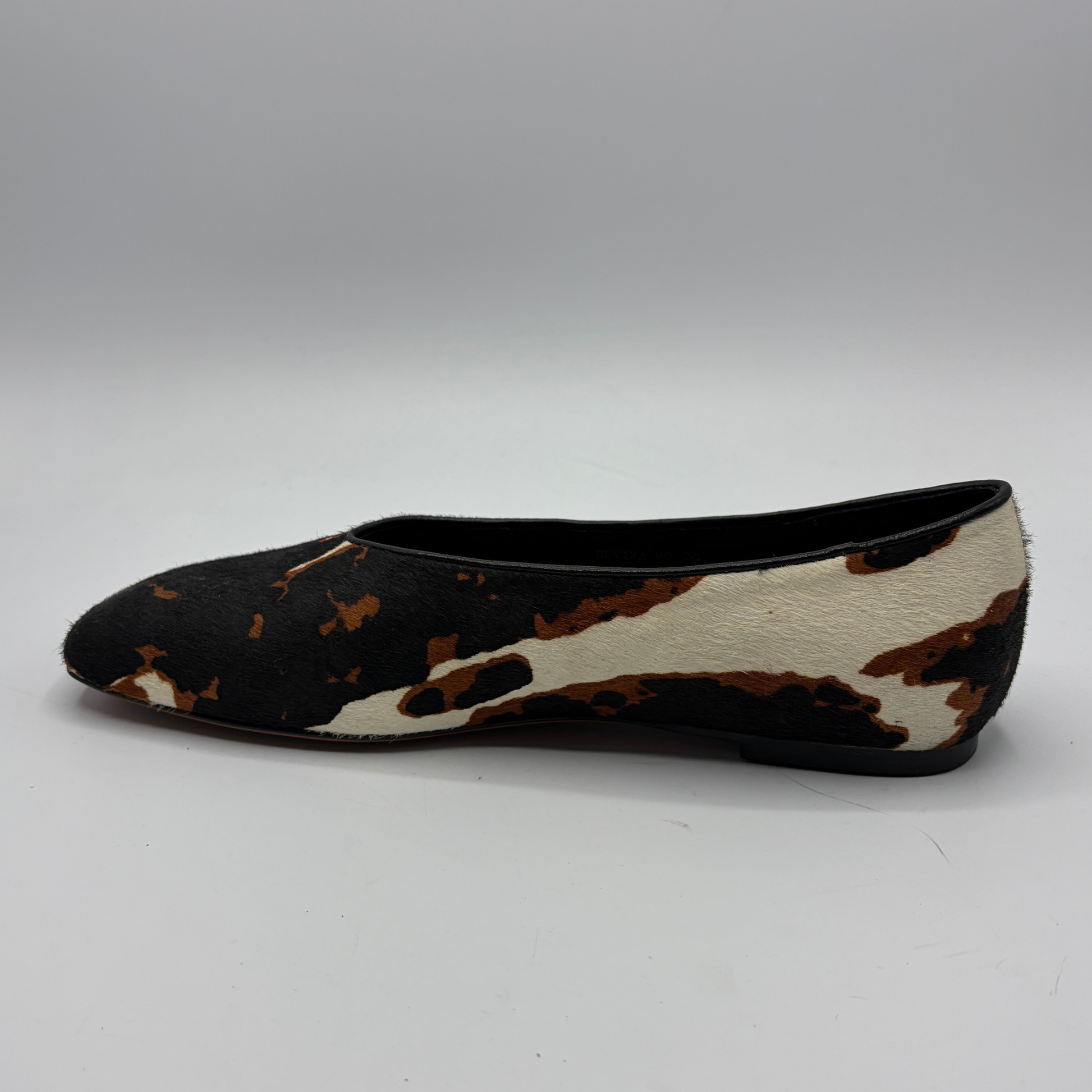 Black and white cow print flat shoe on a gray background