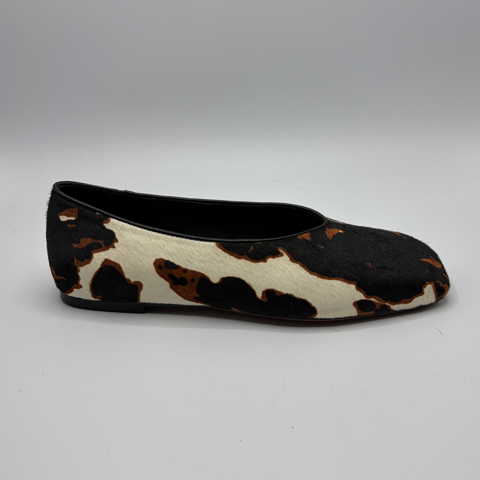 Black and white cowhide patterned flat shoe on a gray background