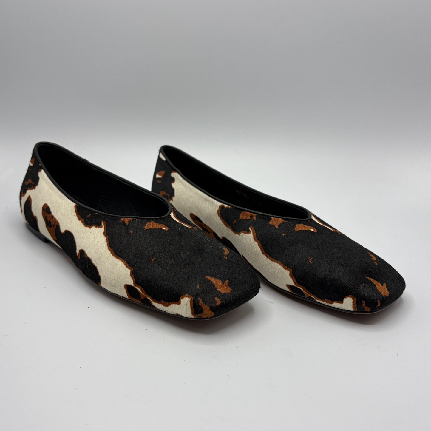 Pair of cow print patterned shoes on a gray background