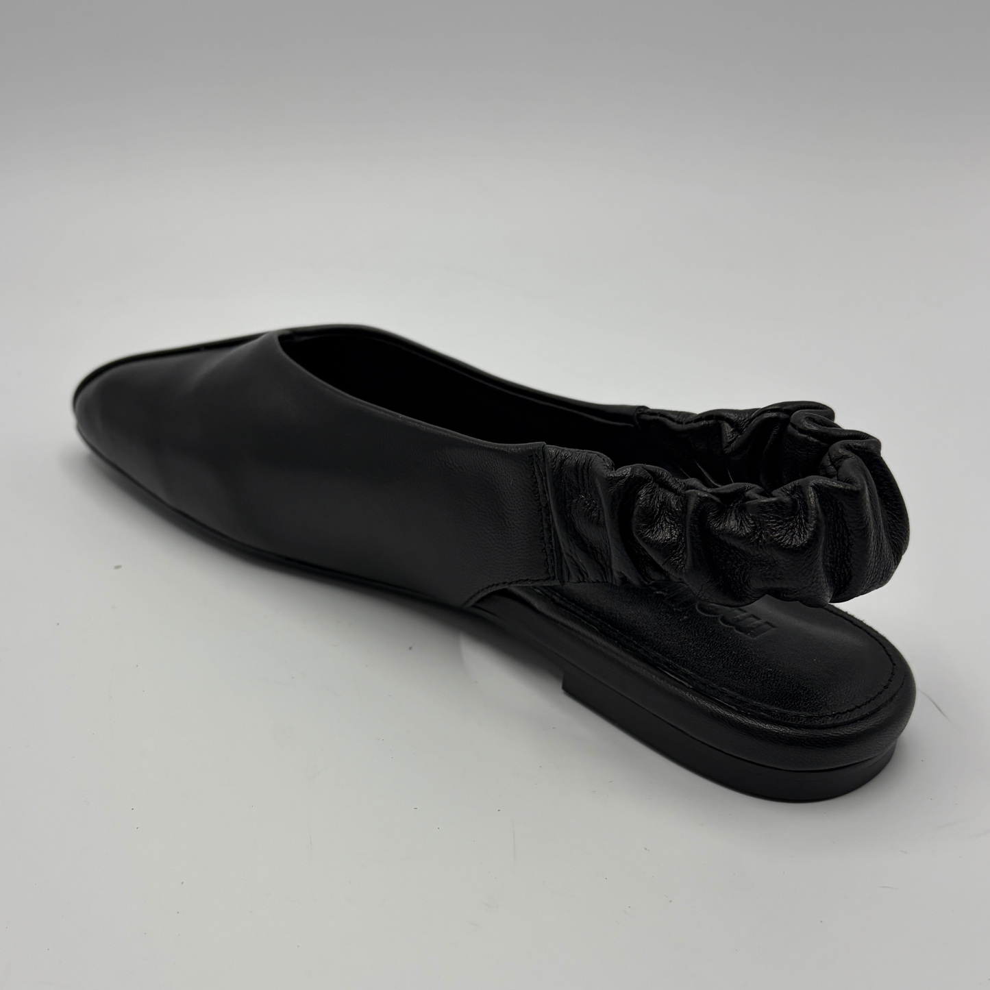 Black flat shoe with ruffled detail on a white background