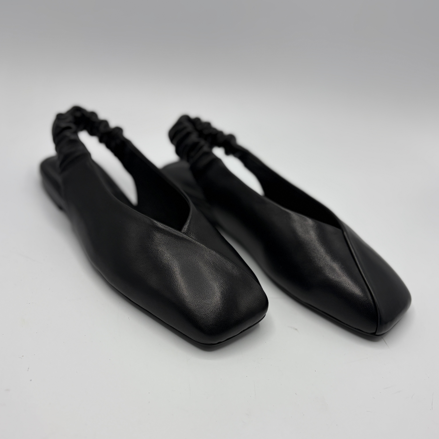 Pair of black leather shoes with square toes on a light gray background