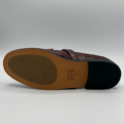 The outsole view of a burgundy crocodile-embossed leather loafer, showing a tan midsole with printed specifications and a black rubber outsole.