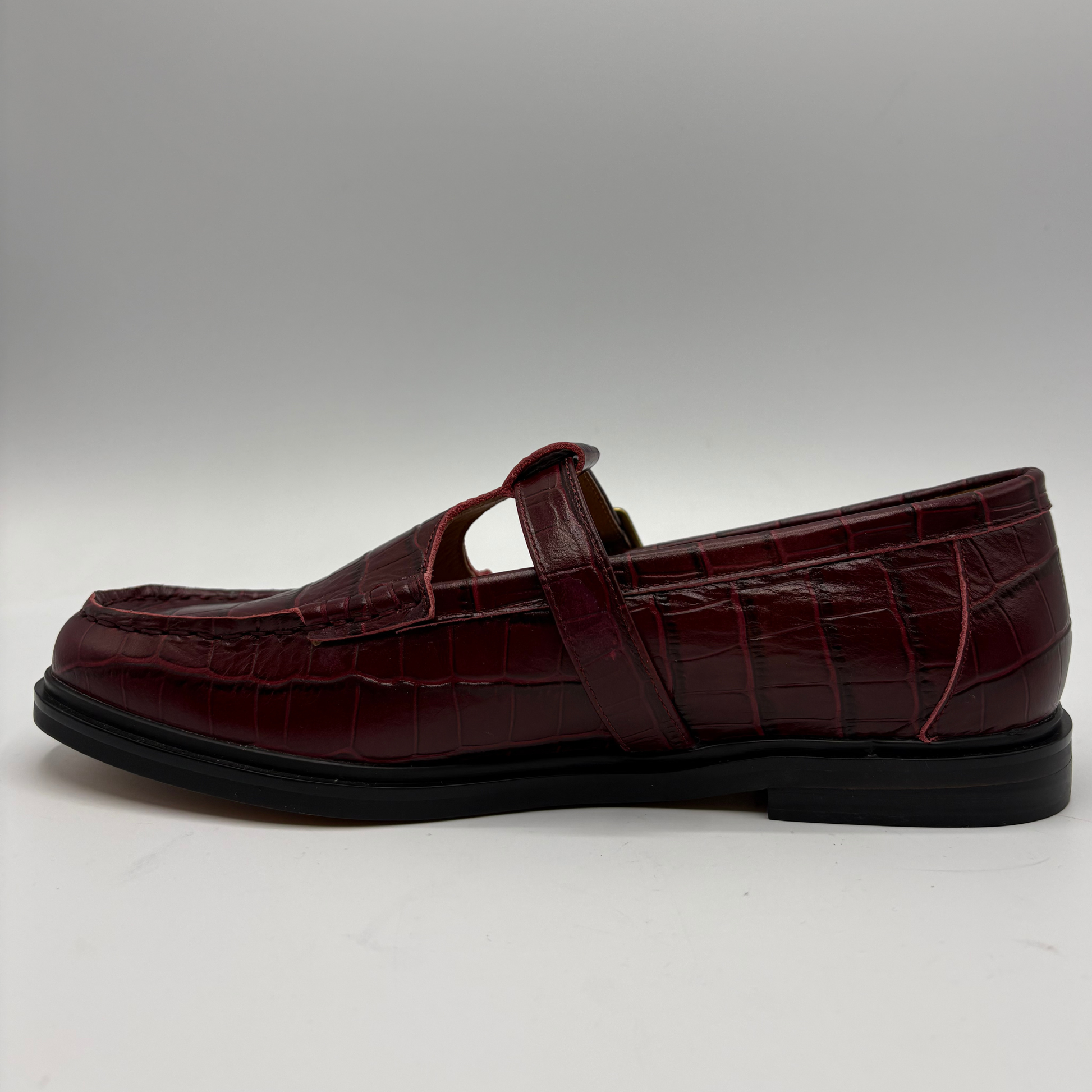 A single dark burgundy crocodile-embossed leather loafer Mary Jane shoe with a black sole, shown in a side profile against a neutral gray background.